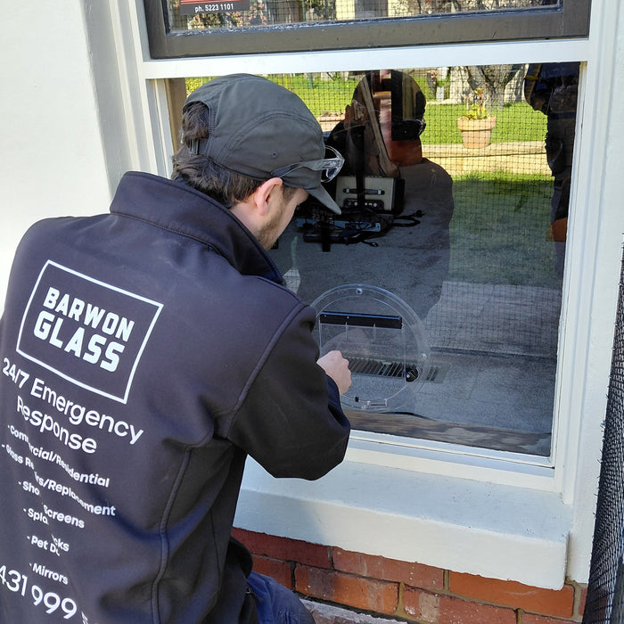 Barwon Glass glazier fitting a round Transcat cat door into the new glass pane in Belmont