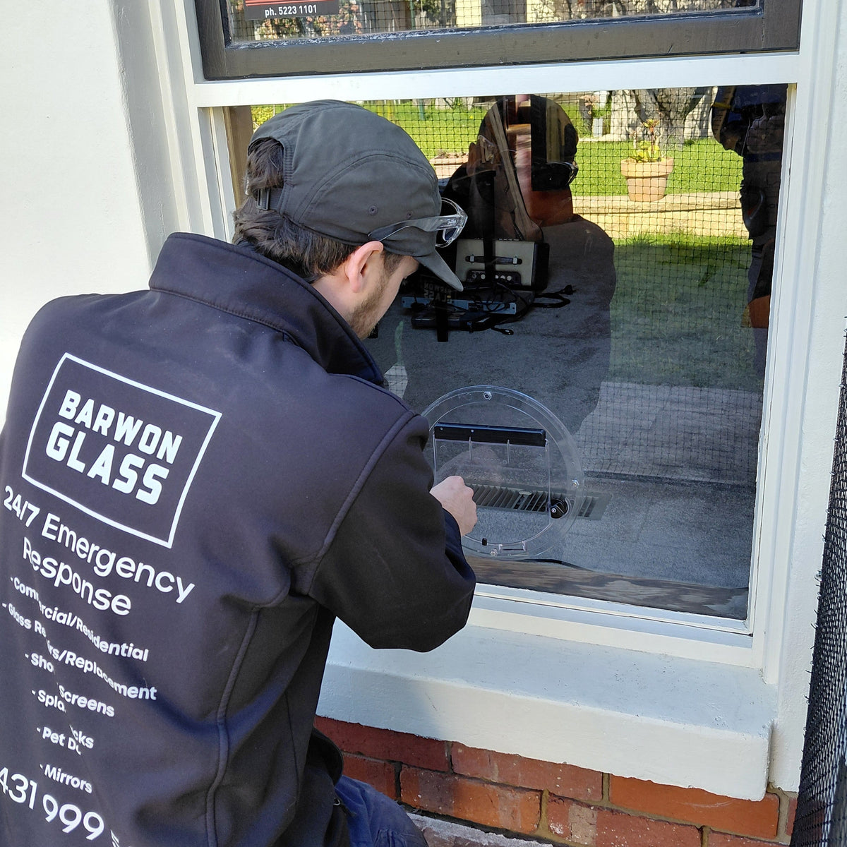 Barwon Glass glazier fitting a round Transcat cat door into the new glass pane in Belmont
