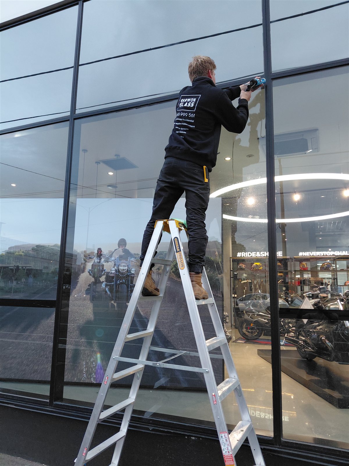 Barwon Glass technician repairing a shopfront window on a ladder